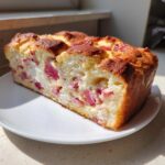 Przekrój puszystego ciasta drożdżowego z rabarbarem i serem na białym talerzyku.