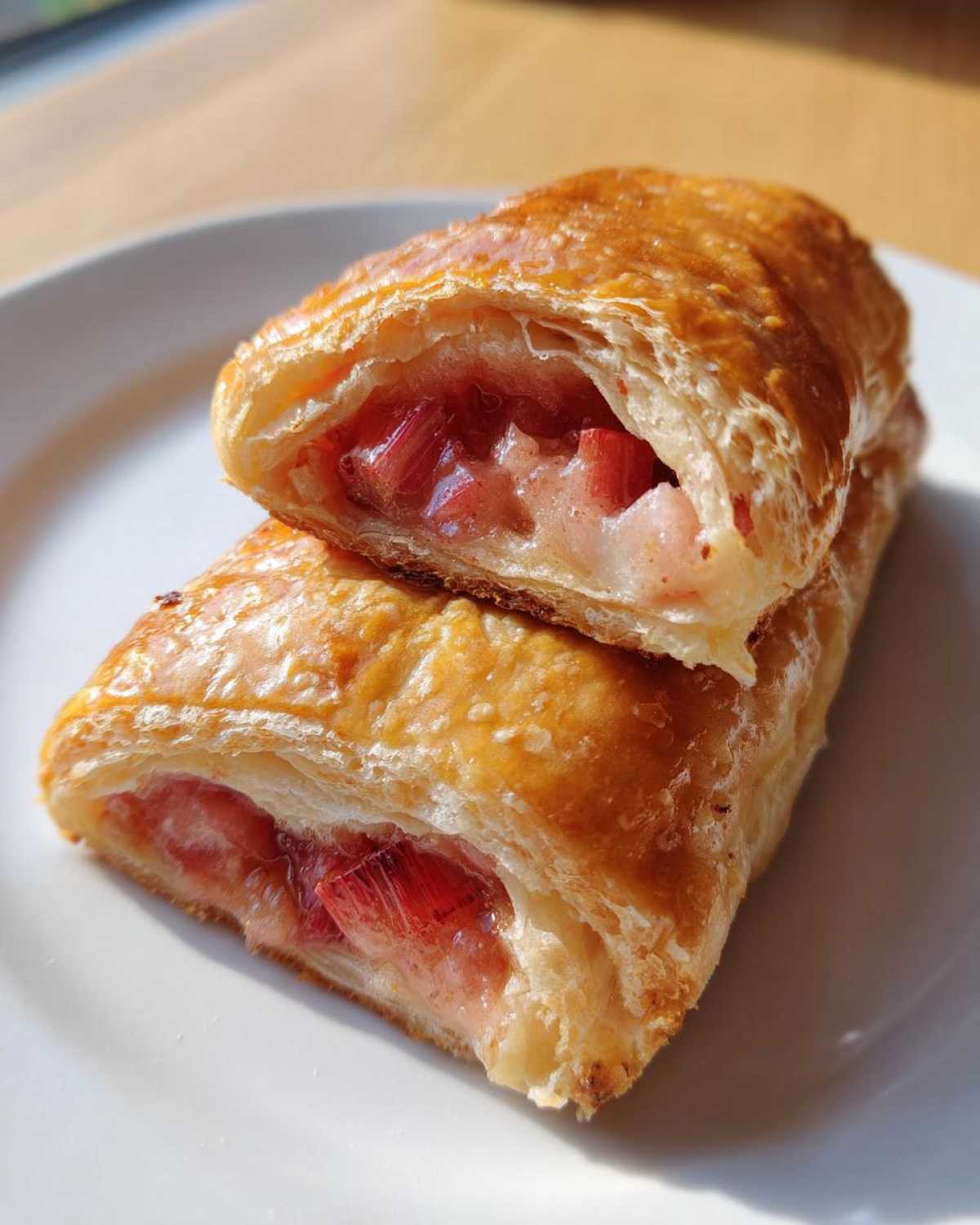 Zbliżenie na przekrojone Ciasto francuskie z rabarbarem, ukazujące złocistą, listkującą się strukturę i różowe kawałki nadzienia.