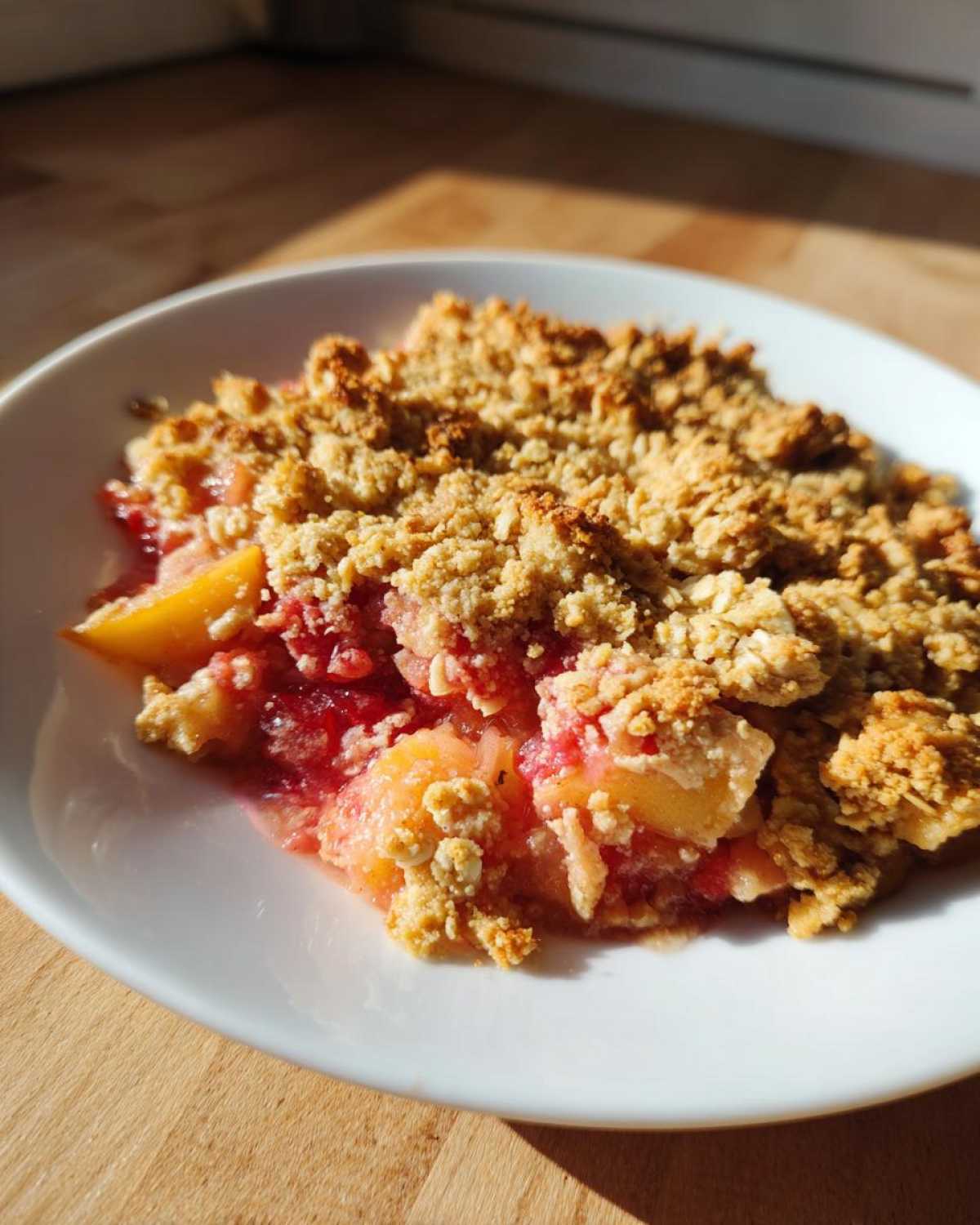 Zbliżenie na porcję chrupiącego Crumble z rabarbarem i jabłkami w białej miseczce.