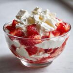 Warstwowy deser Eton mess z truskawkami, bitą śmietaną i kawałkami bezy w szklanym pucharku.
