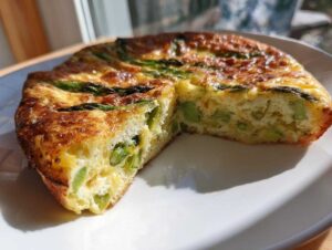 Przekrojona na pół puszysta Frittata ze szparagami na białym talerzu, złocista i apetyczna.