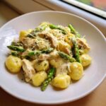 Zbliżenie na talerz z Gnocchi z kurczakiem i szparagami w kremowym sosie, posypane parmezanem.
