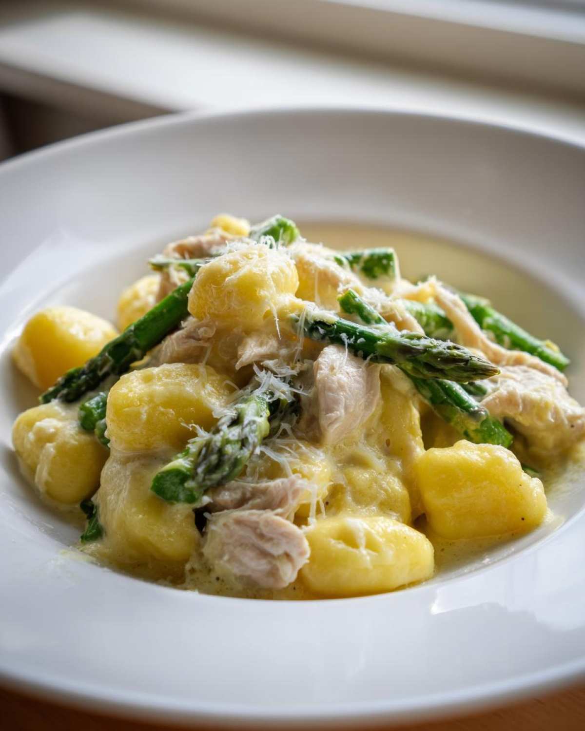 Zbliżenie na talerz Gnocchi z kurczakiem i szparagami w kremowym sosie, posypane parmezanem.