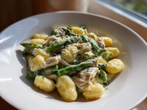 Talerz pełen Gnocchi z kurczakiem i szparagami w kremowym sosie, posypane parmezanem.