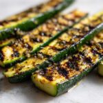Zbliżenie na paski grillowanej cukinii z oliwą i czosnkiem, widoczne ślady przypieczenia.