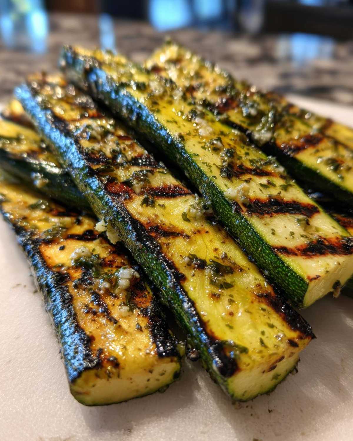 Zbliżenie na paski grillowanej cukinii z oliwą i czosnkiem, widoczne ślady po grillu.
