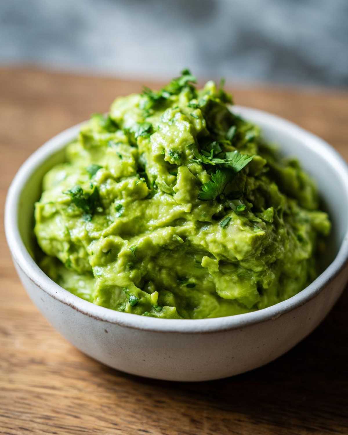 Zbliżenie na miseczkę z kremowym, zielonym guacamole do mięs z grilla, posypane kolendrą.