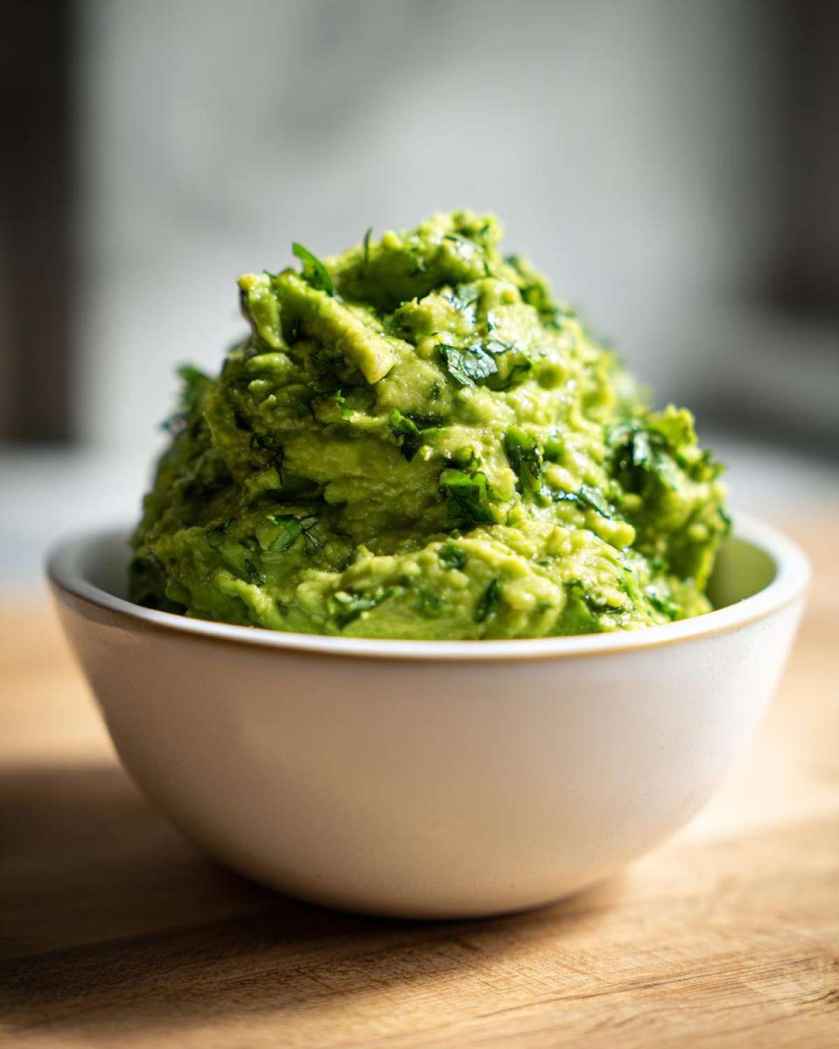 Gęste, zielone guacamole do mięs z grilla z kawałkami ziół w białej miseczce.