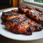 Zbliżenie na grillowaną karkówkę z przypieczoną skórką, ułożoną na białym talerzu.