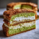 Zbliżenie na przekrój ciasta Karpatka pistacjowa z warstwami zielonego biszkoptu, kremu i chrupiącej kruszonki.