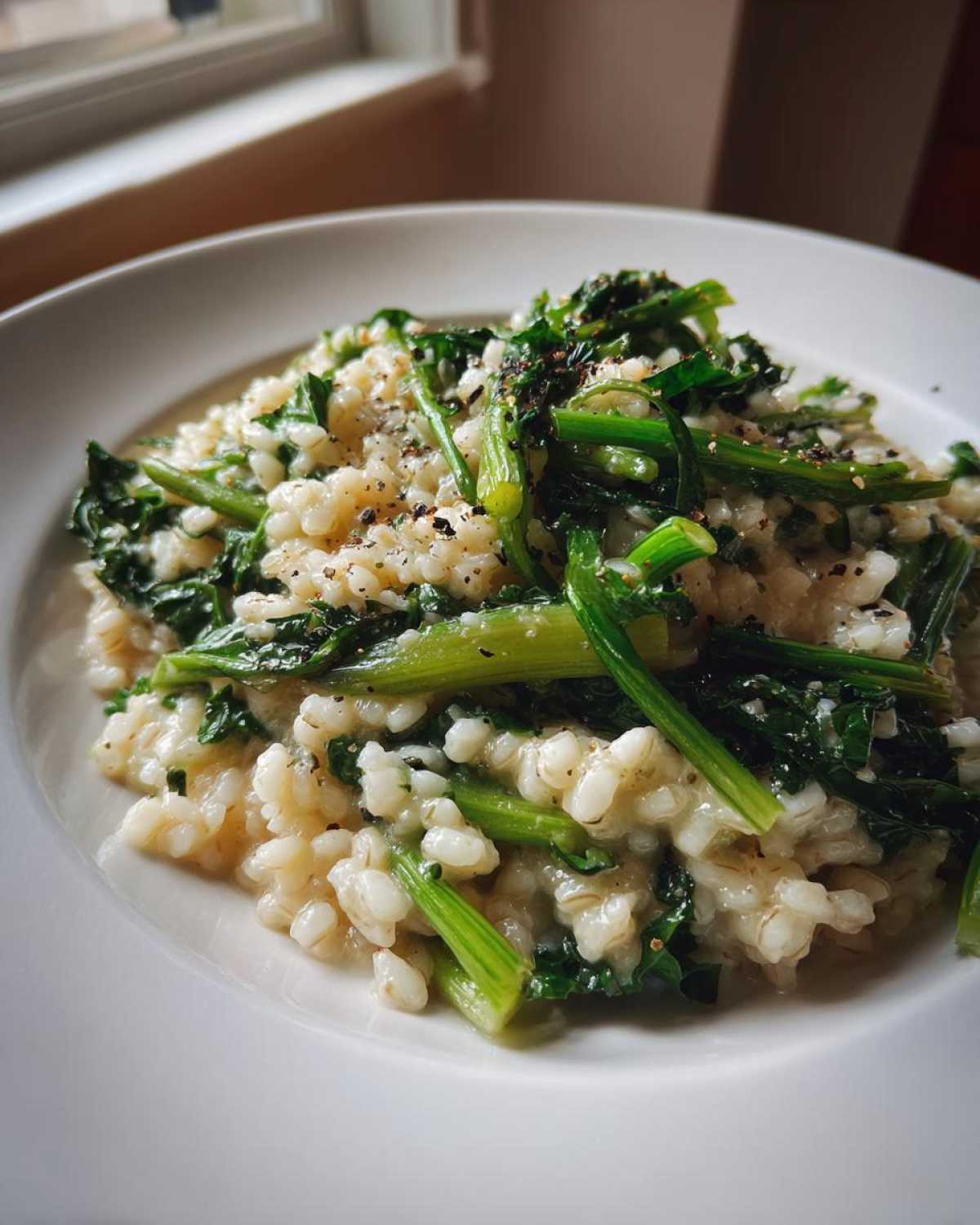 Kremowe kaszotto warzywne z botwinką posypane świeżo mielonym pieprzem w białej misce.