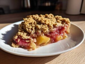 Kawałek puszystego crumble z rabarbarem i jabłkami na białym talerzyku.