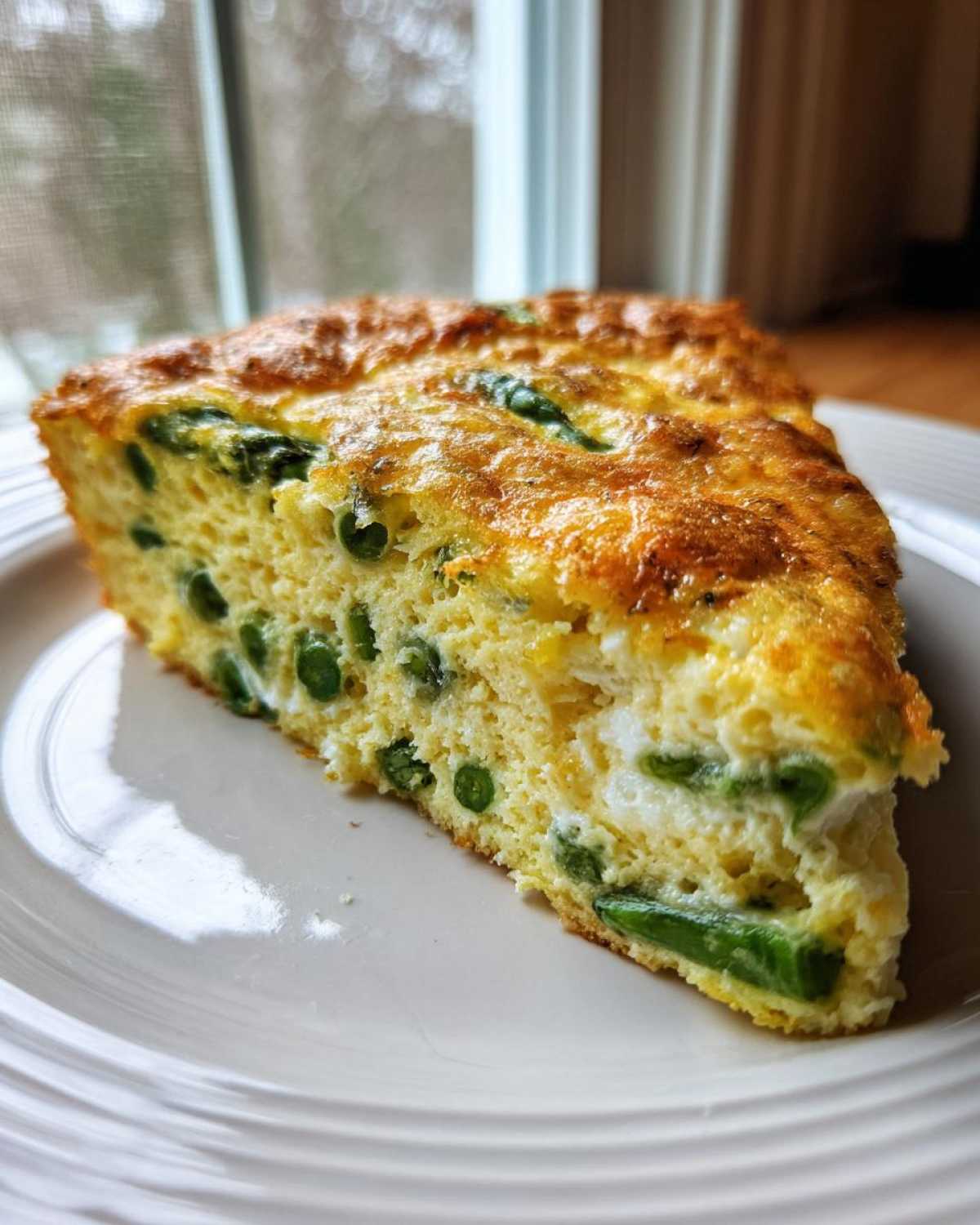 Kawałek puszystej Frittata ze szparagami i groszkiem na białym talerzu.