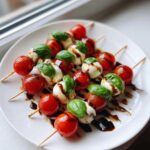 Zbliżenie na koreczki caprese z kulkami mozzarelli, pomidorkami koktajlowymi i bazylią, polane sosem balsamicznym.