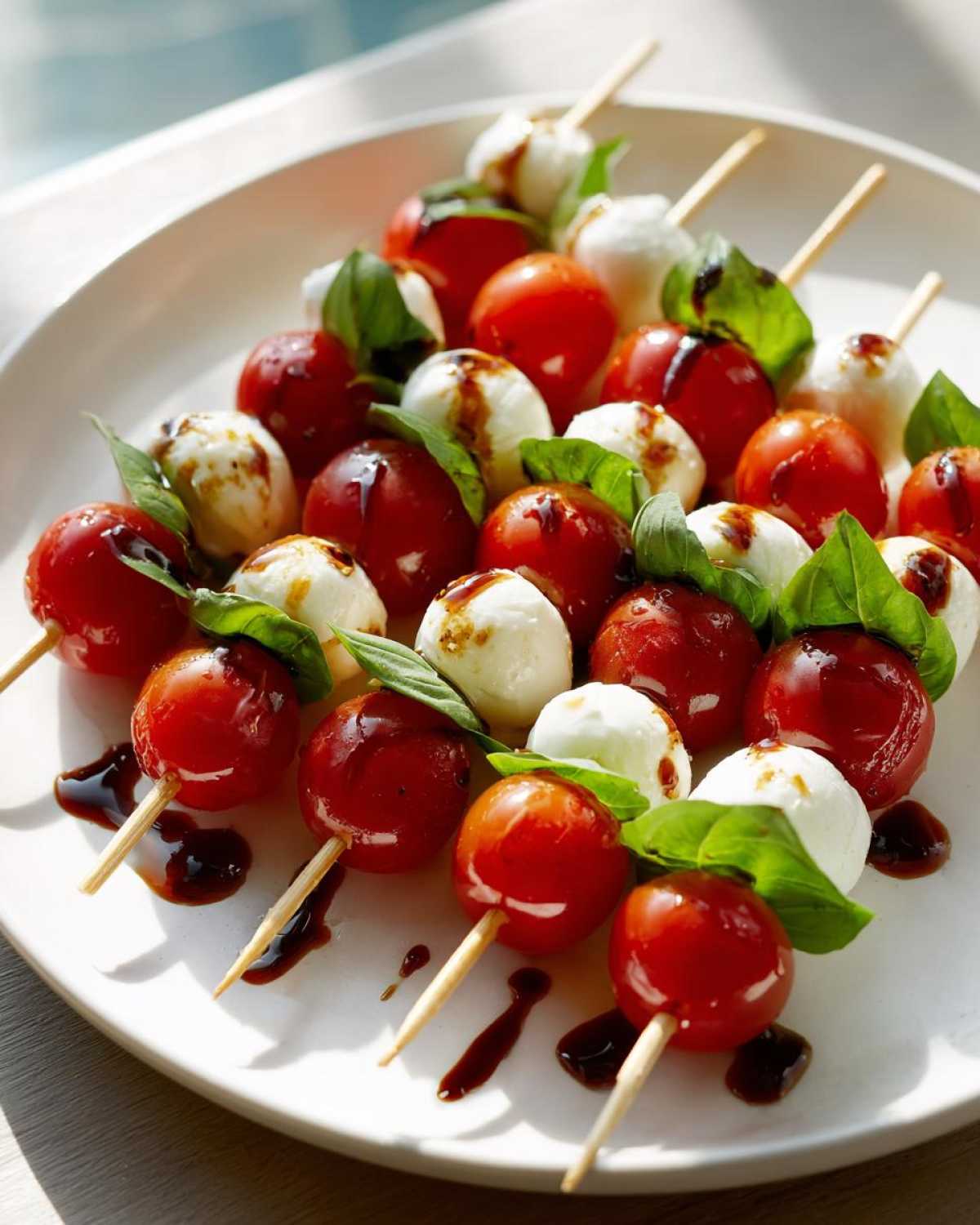 Zbliżenie na koreczki caprese z kulkami mozzarelli, pomidorkami koktajlowymi i bazylią polane sosem balsamicznym.