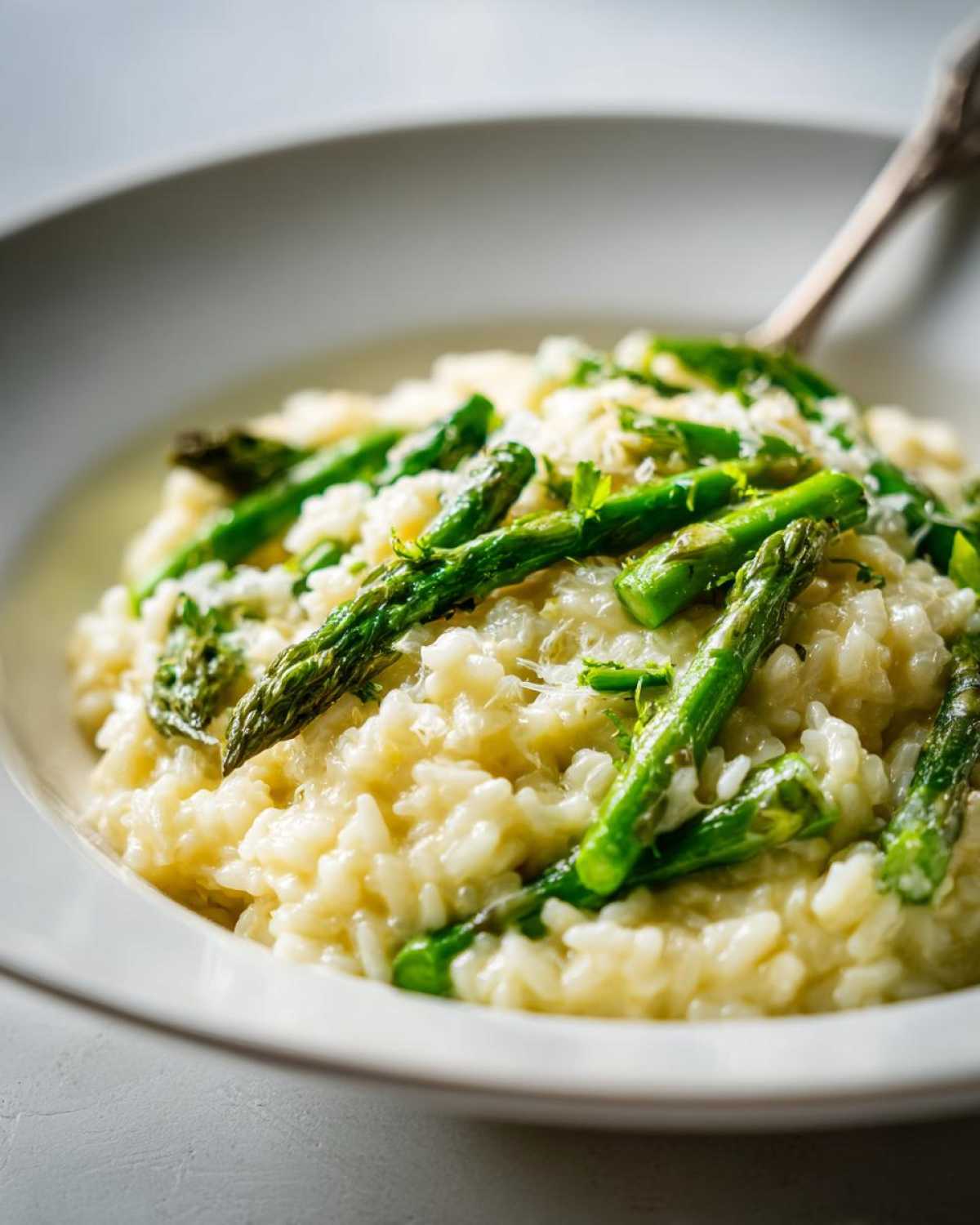 Zbliżenie na kremowe Risotto z zielonymi szparagami posypane parmezanem w białej misce.
