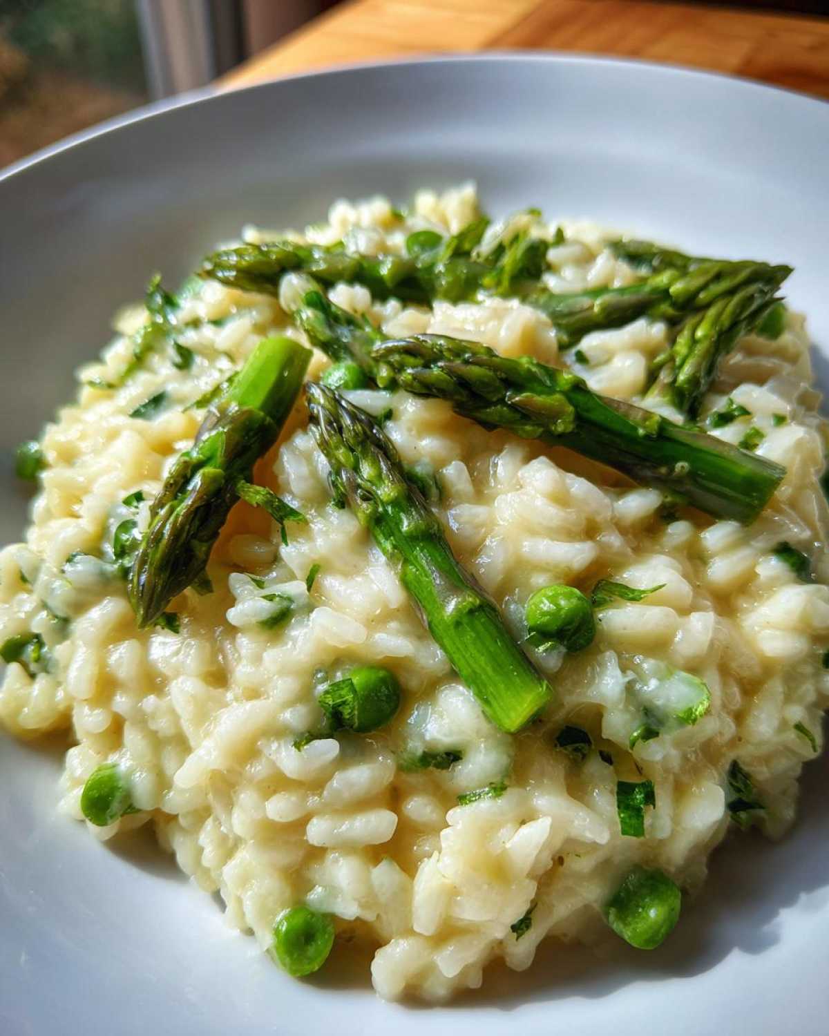 Zbliżenie na kremowe Risotto z zielonymi szparagami i groszkiem podane w białej misce.