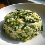 Kremowe Risotto ze szparagami podane w białej misce, z widocznymi kawałkami zielonych szparagów.
