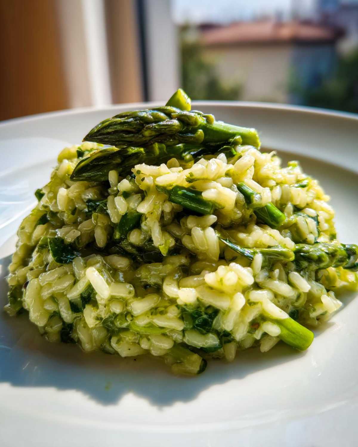 Zbliżenie na porcję kremowego Risotto ze szparagami, udekorowane całą zieloną szparagą.