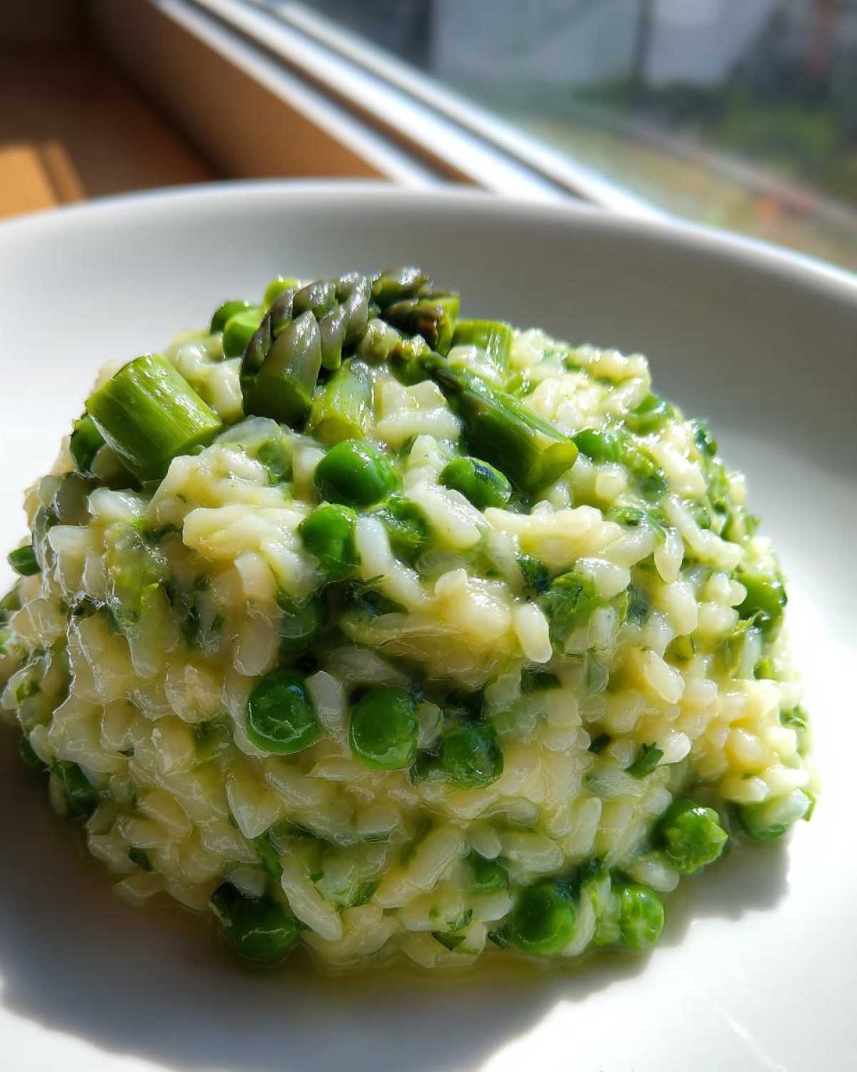 Zbliżenie na porcję kremowego Risotto ze szparagami i zielonym groszkiem na białym talerzu.