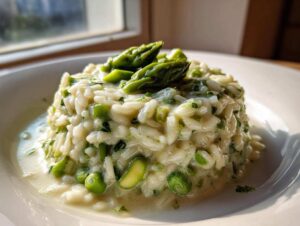 Kremowe Risotto ze szparagami podane na białym talerzu, udekorowane wierzchołkami szparagów.