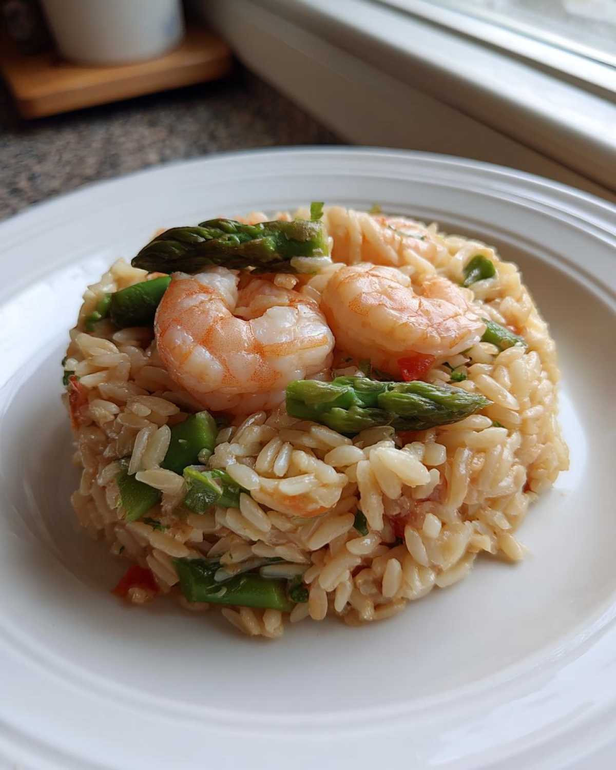 Zbliżenie na porcję Makaron orzo z krewetkami i szparagami podaną na białym talerzu.