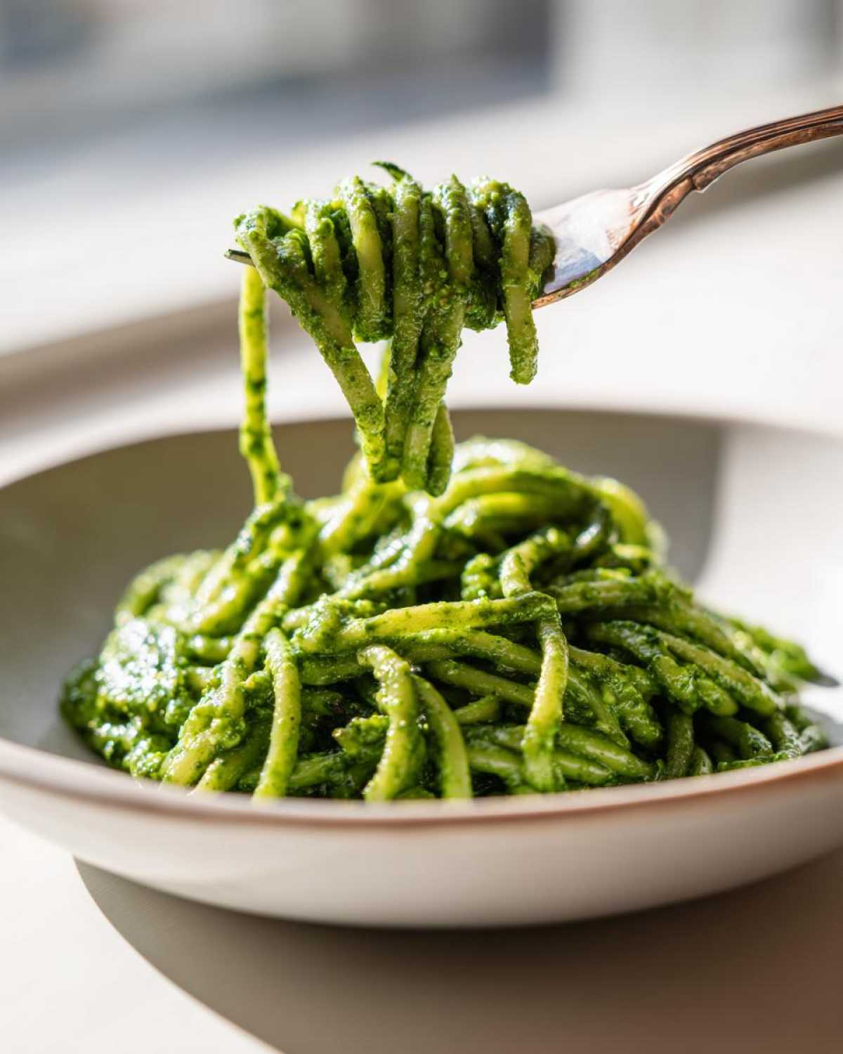 Widelec podnosi porcję makaronu obficie polanego intensywnie zielonym Pesto z liści botwinki.