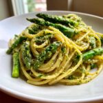 Zbliżenie na talerz Makaron z pesto pistacjowym i szparagami, posypany tartym serem.