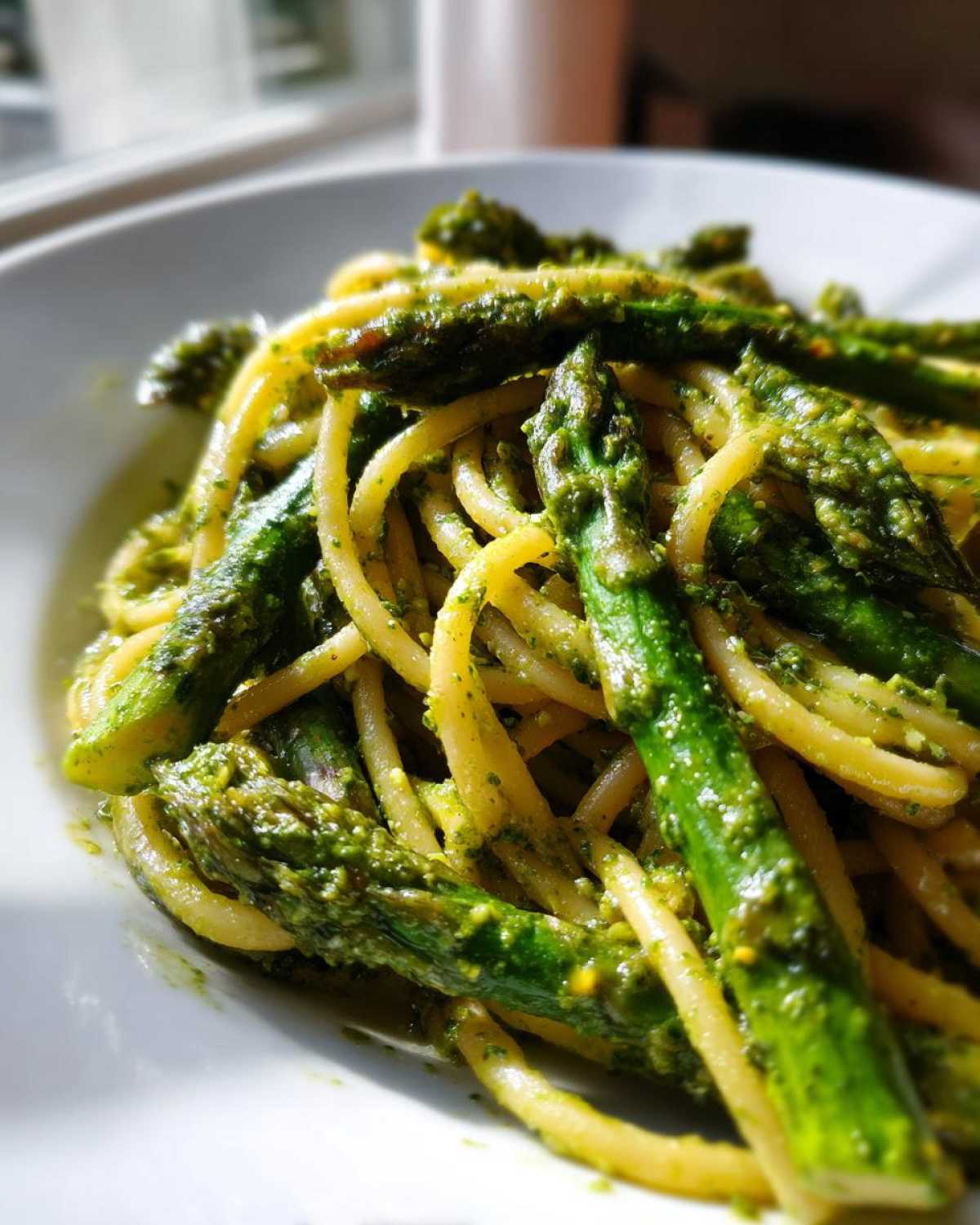 Zbliżenie na makaron z pesto pistacjowym i zielonymi szparagami podane na białym talerzu.