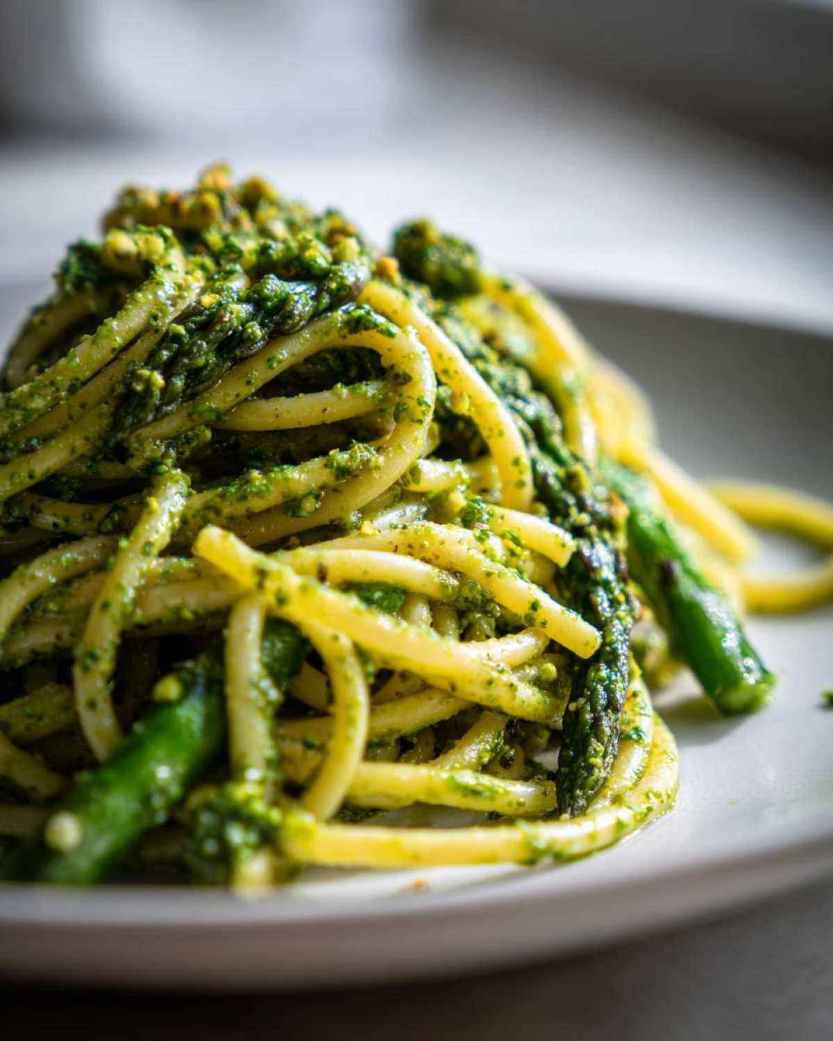 Zbliżenie na porcję makaronu z pesto pistacjowym i kawałkami szparagów na białym talerzu.
