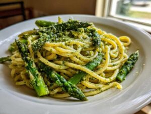Zbliżenie na makaron z pesto pistacjowym i szparagami, obficie polany sosem i posypany serem.