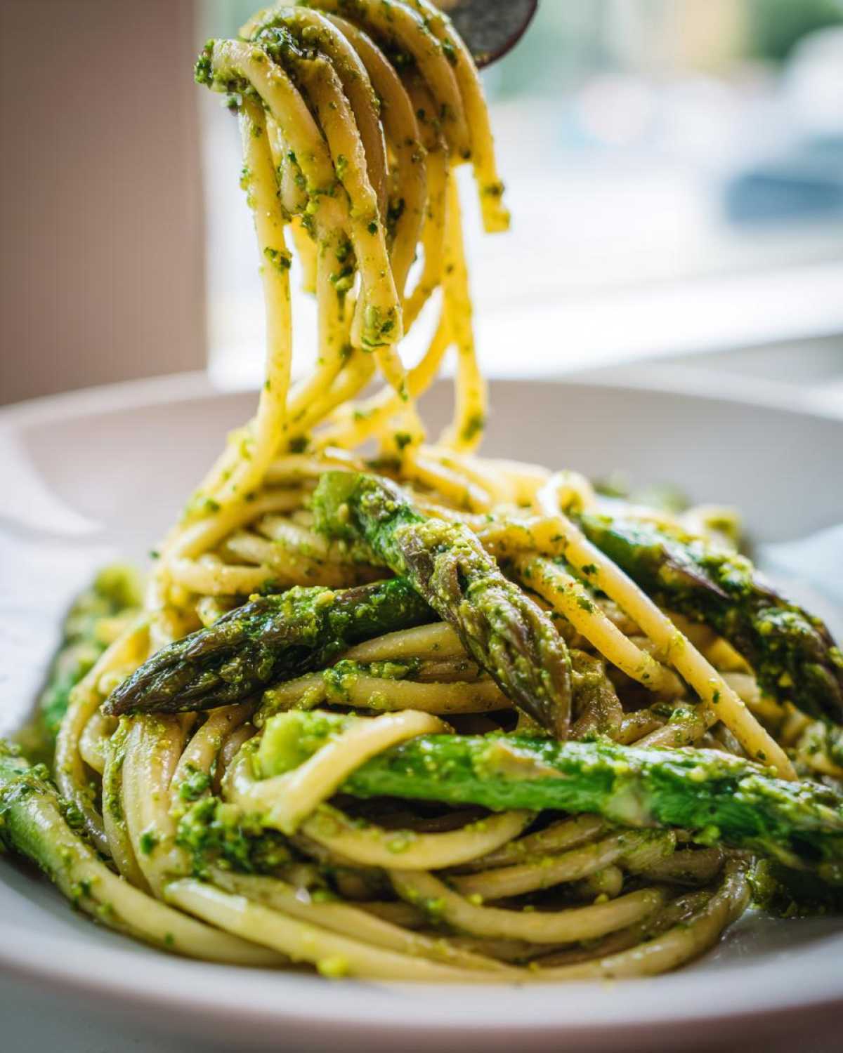 Zbliżenie na makaron z pesto pistacjowym i szparagami, część porcji jest podnoszona widelcem.