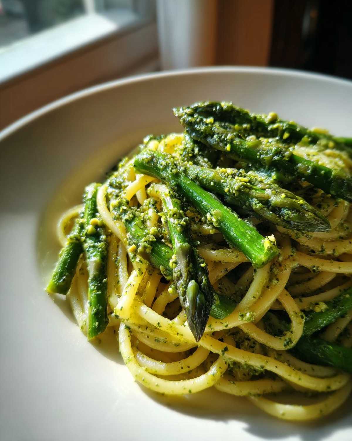 Zbliżenie na makaron z pesto pistacjowym i gotowanymi szparagami podane w białej misce.