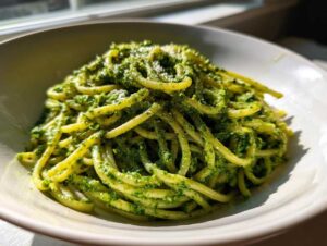 Miseczka makaronu spaghetti obficie polana intensywnie zielonym Pesto z liści botwinki.