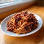Porcja soczystego Pulled pork z wolnowaru na burgery w sosie BBQ na białym talerzu.