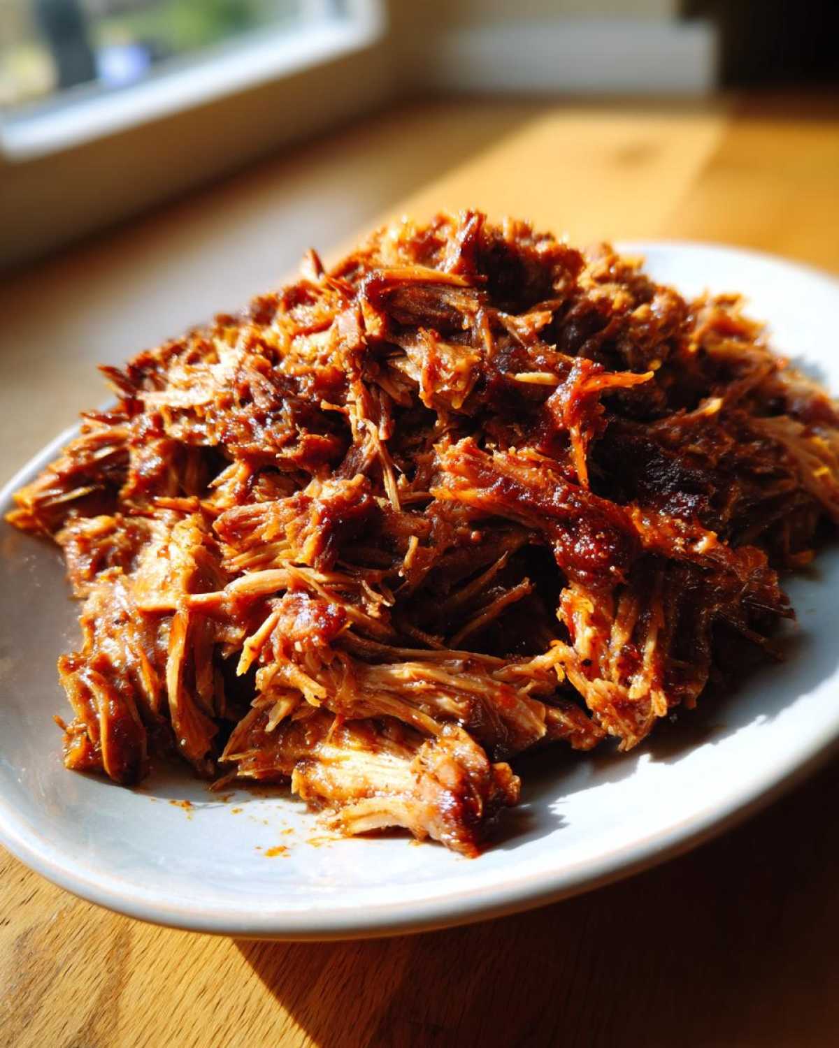 Zbliżenie na soczysty, poszarpany Pulled pork z wolnowaru na burgery na jasnym talerzu.