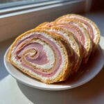 Kilka pokrojonych plastrów Roladki z szynki z chrzanem, widoczny spiralny środek z szynką i kremem.