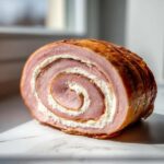 Przekrój Roladki z szynki z nadzieniem chrzanowym, widoczny spiralny wzór szynki i białego kremowego farszu.