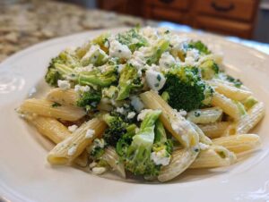 Porcja sałatki makaronowej z brokułami, penne i kawałkami sera feta na białym talerzu.