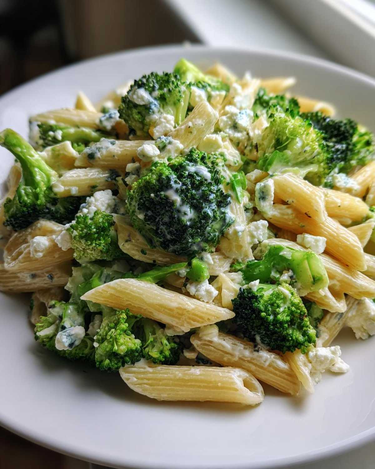 Zbliżenie na talerz pełen penne, brokułów i sera feta/pleśniowego, kluczowy element Sałatka makaronowa z brokułami.