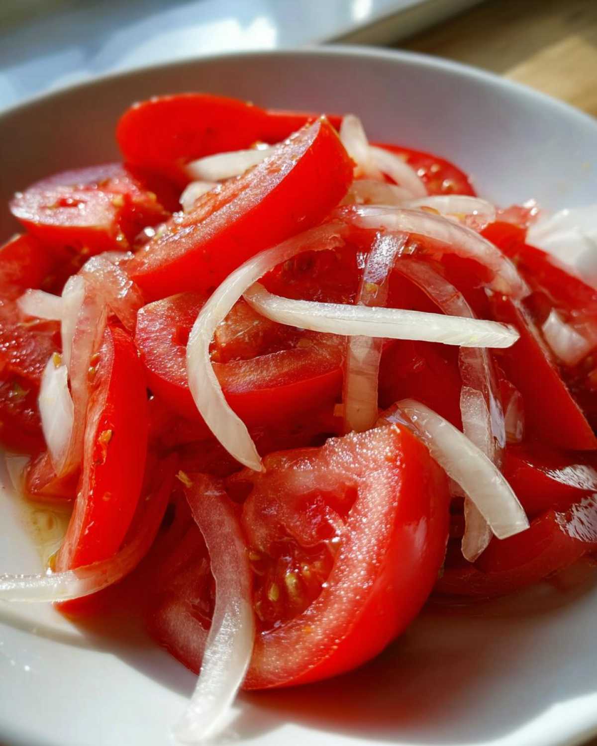 Zbliżenie na miskę z soczystą Sałatką z pomidorów i cebuli, pokrojoną w ćwiartki i wymieszaną z cienkimi plasterkami białej cebuli.