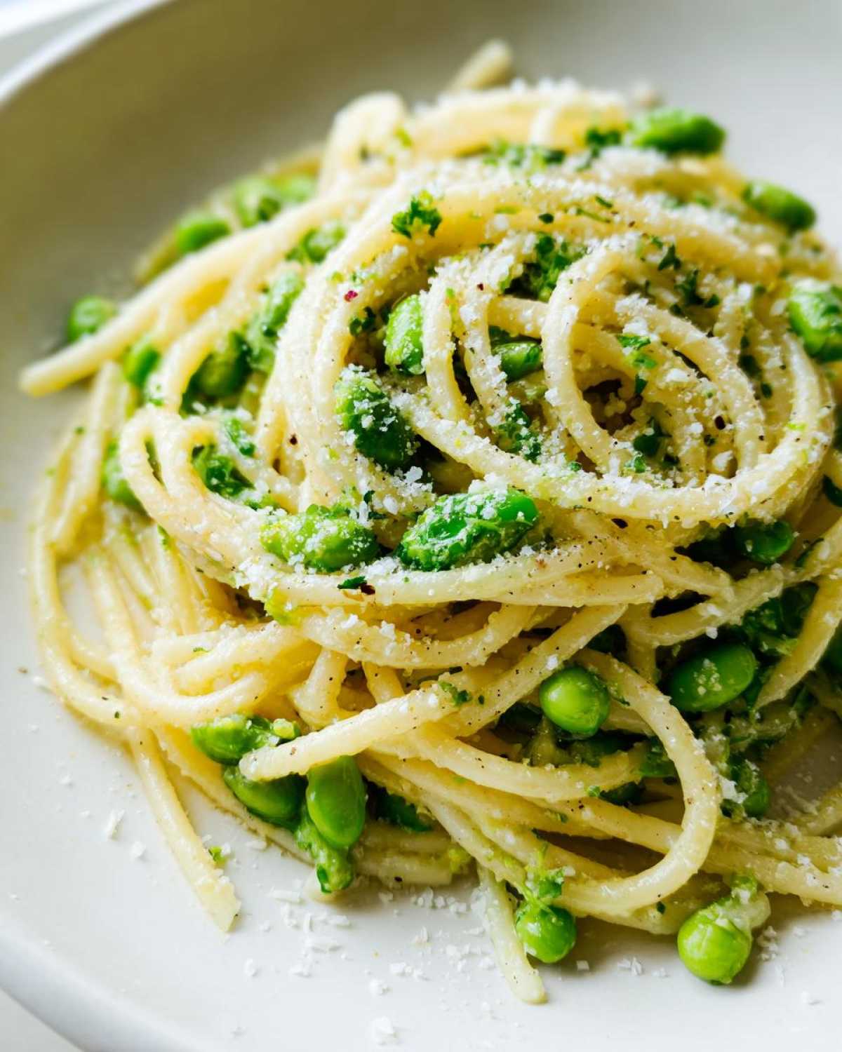 Zbliżenie na porcję Spaghetti z bobem czosnkiem i parmezanem posypane tartym serem.