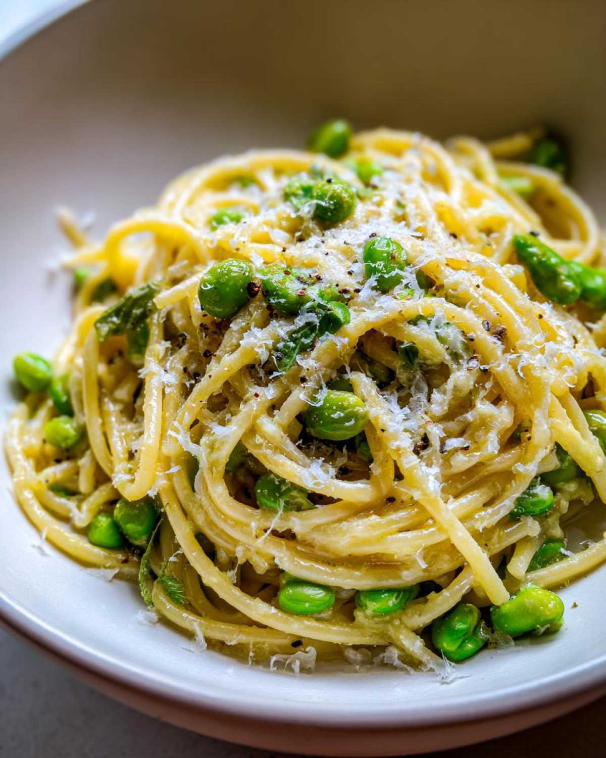 Zbliżenie na talerz pełen Spaghetti z bobem czosnkiem i parmezanem, posypane tartym serem.