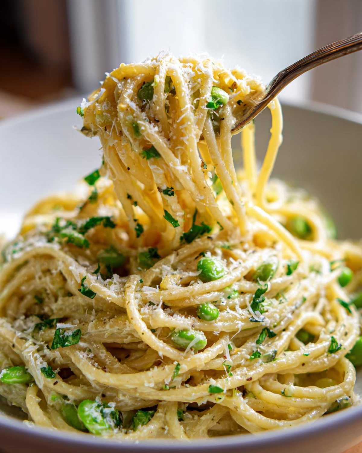 Kluski spaghetti z bobem, czosnkiem i parmezanem nawinięte na widelec.