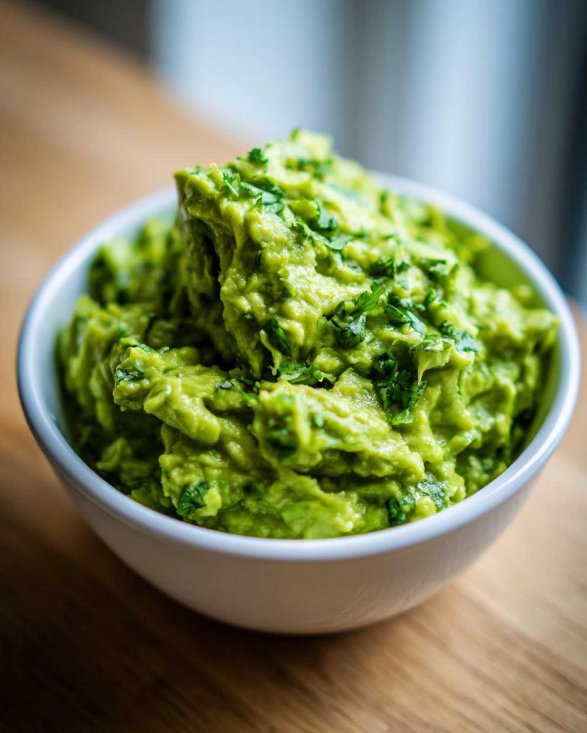 Gęste, zielone Guacamole do mięs z grilla posypane świeżą kolendrą w białej miseczce.