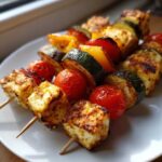 Zbliżenie na grillowane szaszłyki warzywne z serem halloumi, cukinią, papryką i pomidorkami koktajlowymi na białym talerzu.