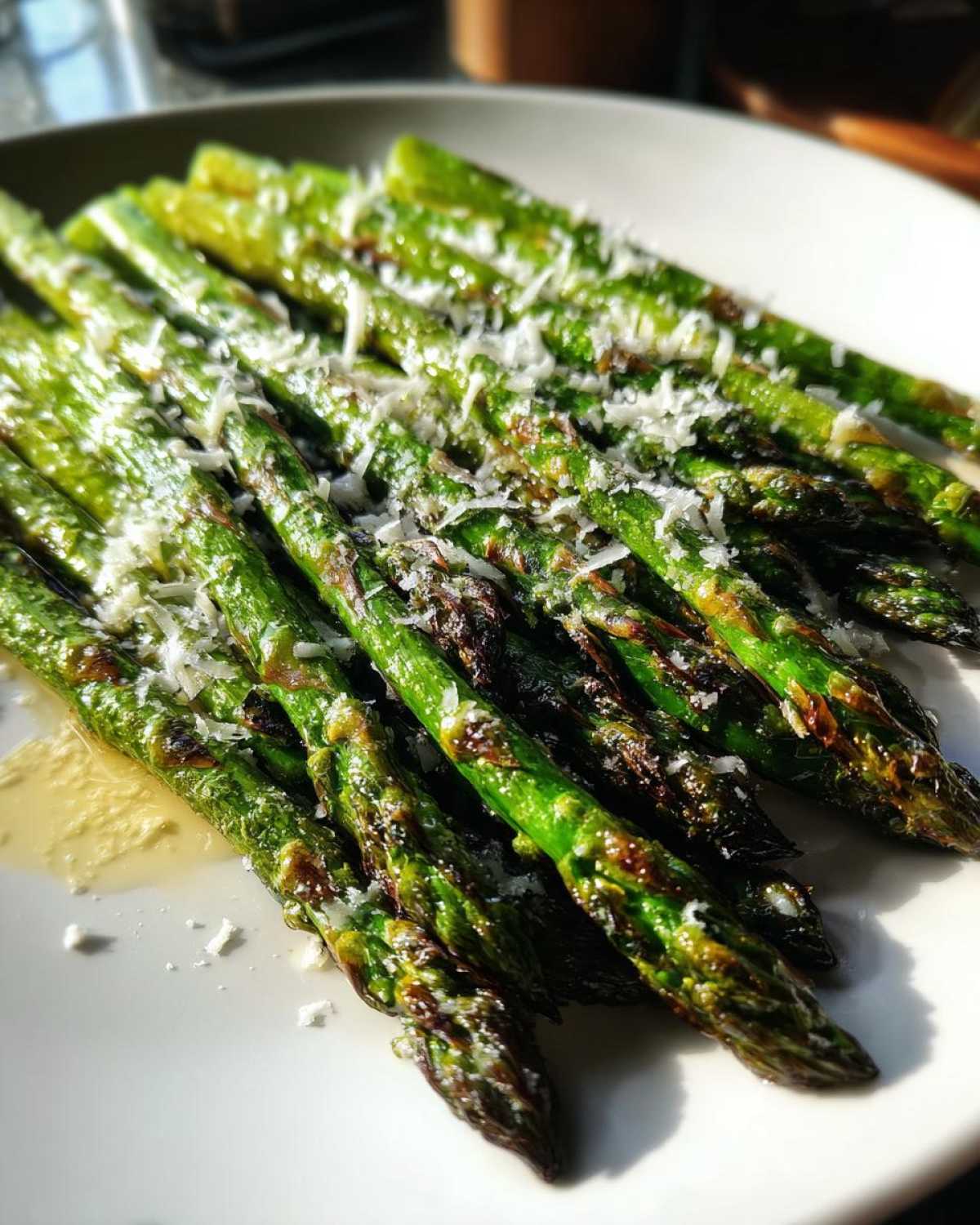 Zbliżenie na grillowane Szparagi z grilla z parmezanem, polane oliwą na białym talerzu.