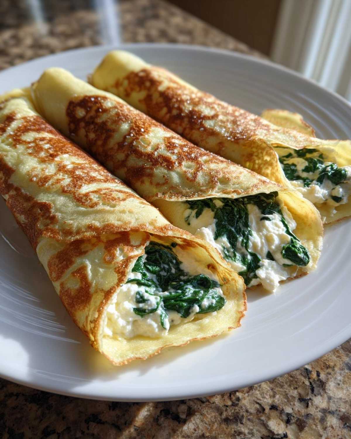 Trzy zwinięte naleśniki wypełnione szpinakiem i serem feta, ułożone na białym talerzu.