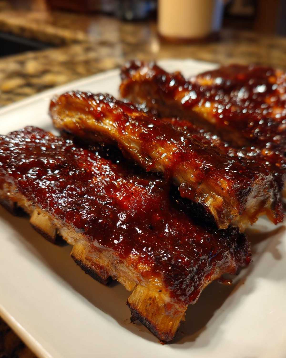 Zbliżenie na soczyste żeberka BBQ z grilla, obficie polane błyszczącym, ciemnym sosem.