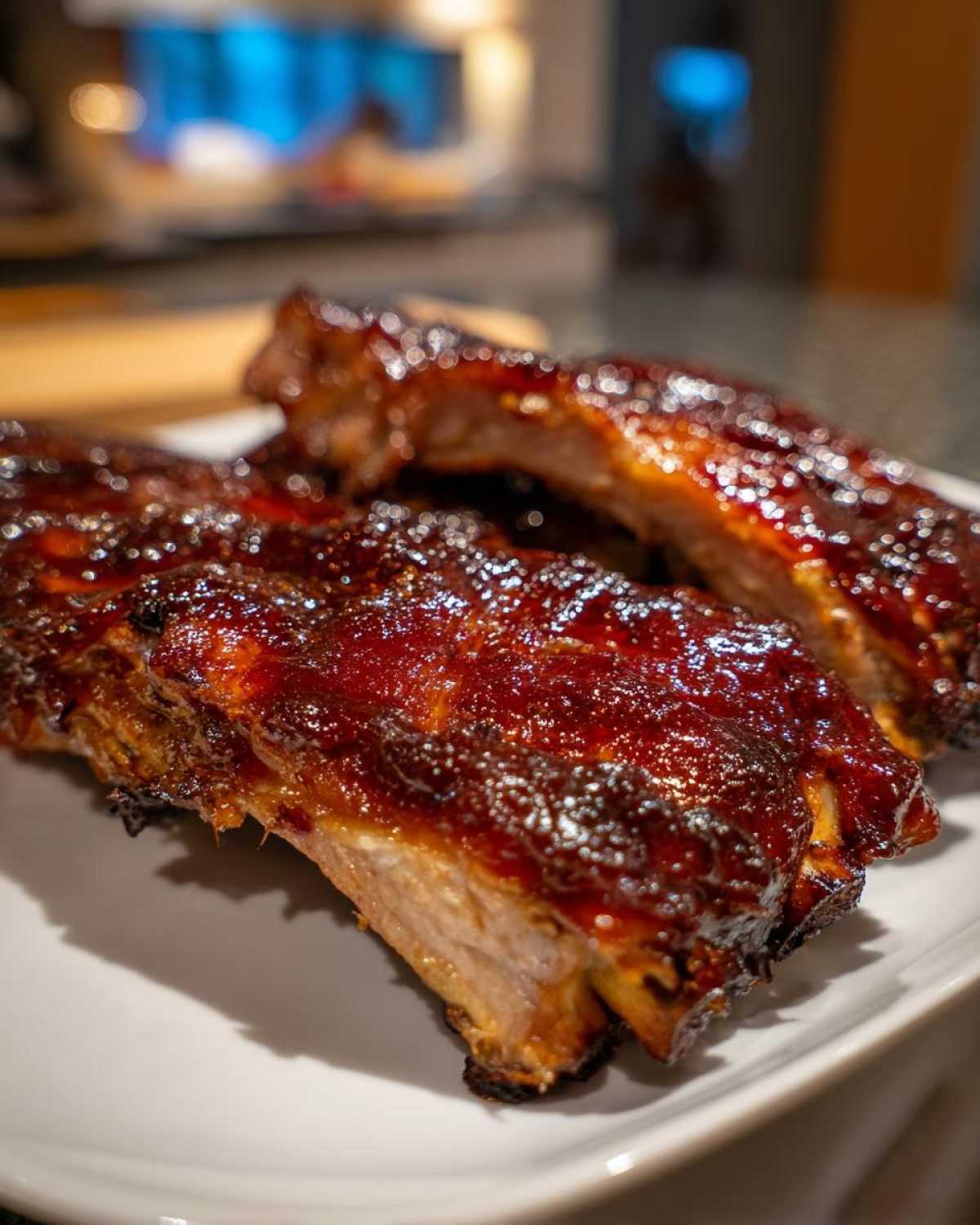 Zbliżenie na soczyste żeberka BBQ z grilla pokryte błyszczącym, karmelowym sosem na białym talerzu.